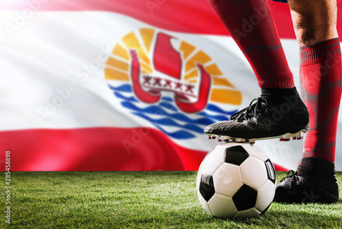 Close up legs of French Polynesia football team player in red socks, shoes on soccer ball at the free kick or penalty spot playing on grass.