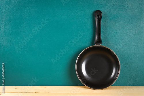 Fényképezés Black frying pan on a wooden shelf on teal background