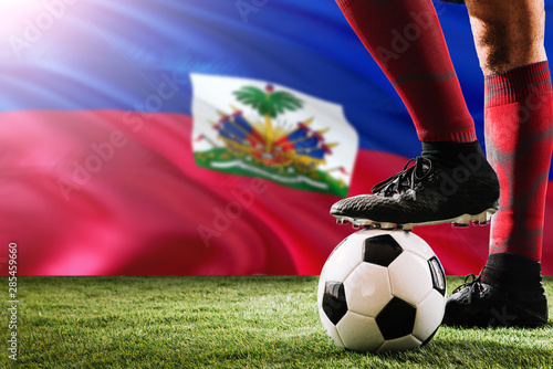 Close up legs of Haiti football team player in red socks, shoes on soccer ball at the free kick or penalty spot playing on grass.