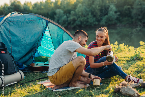 young couple on camping by the river drinking tea or coffee