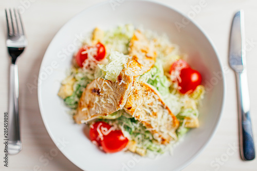 Fresh healthy caesar salad with chicken on white wooden table with fork and knife. Top view. Selective focus.