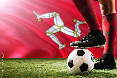 Close up legs of Isle Of Man football team player in red socks  shoes on soccer ball at the free kick or penalty spot playing on grass.