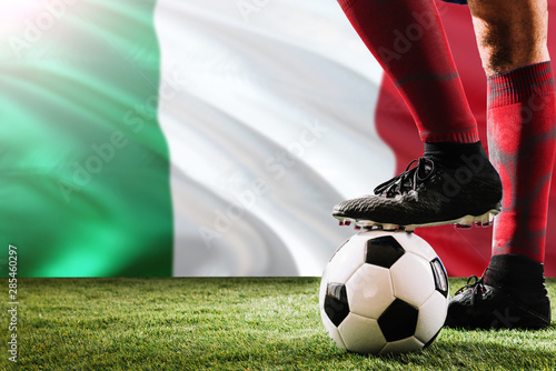 Close up legs of Italy football team player in red socks, shoes on soccer ball at the free kick or penalty spot playing on grass.