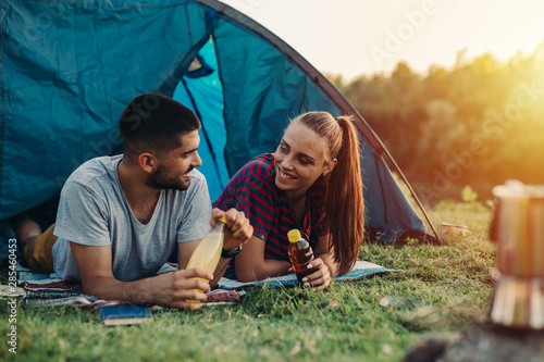 young couple talking and drinking juice while camping outdoor