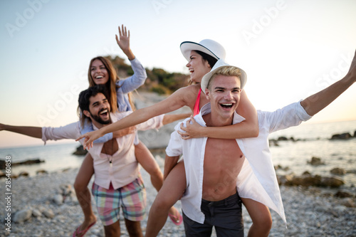 Group of friends having fun on the beach under sunset on vacation