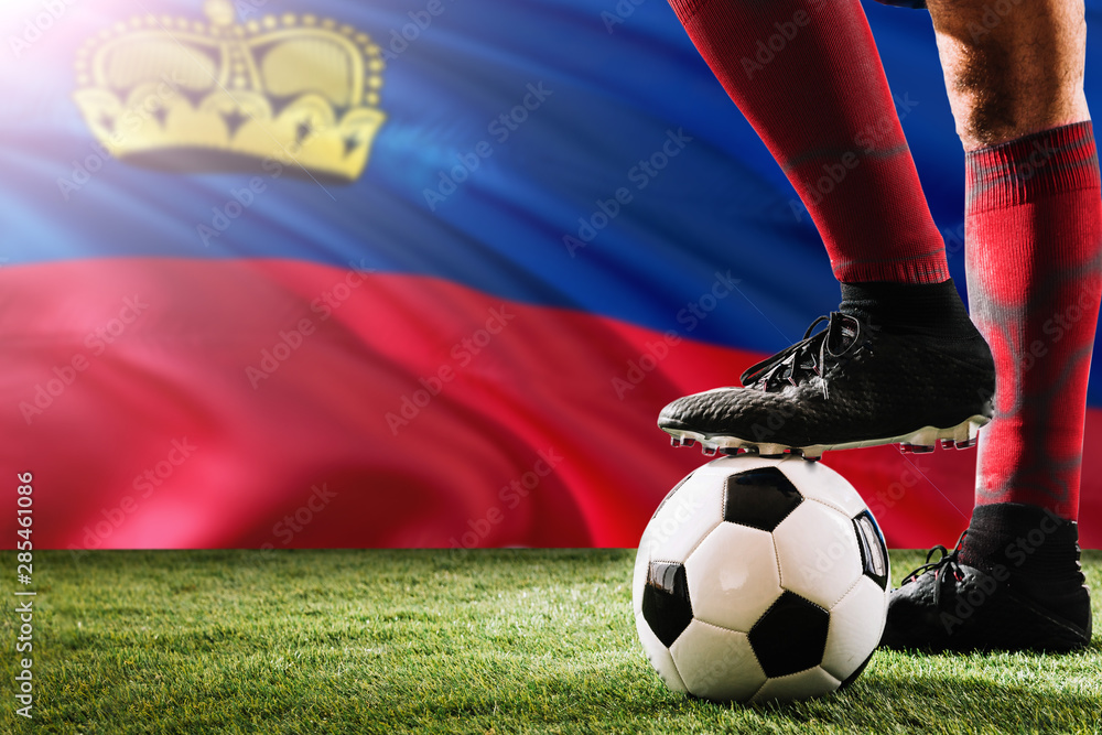Close up legs of Liechtenstein football team player in red socks, shoes on soccer ball at the free kick or penalty spot playing on grass.