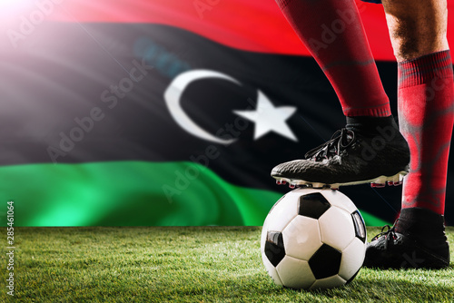 Close up legs of Libya football team player in red socks, shoes on soccer ball at the free kick or penalty spot playing on grass.