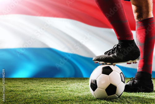Close up legs of Luxembourg football team player in red socks, shoes on soccer ball at the free kick or penalty spot playing on grass.