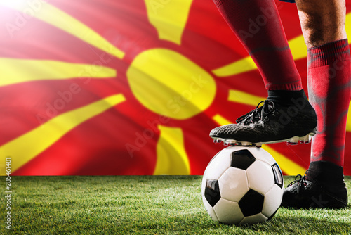 Close up legs of Macedonia football team player in red socks, shoes on soccer ball at the free kick or penalty spot playing on grass.
