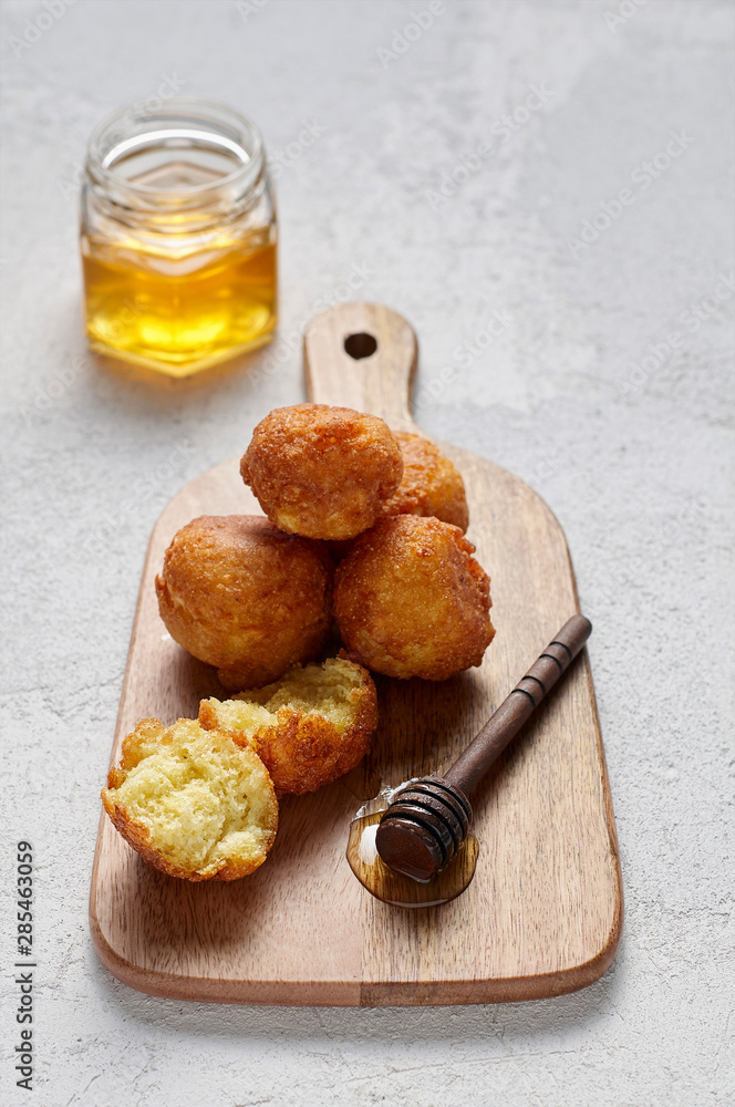 Cottage cheese balls doughnuts is jam-packed with jelly filling on wooden cut board and glass jar honey