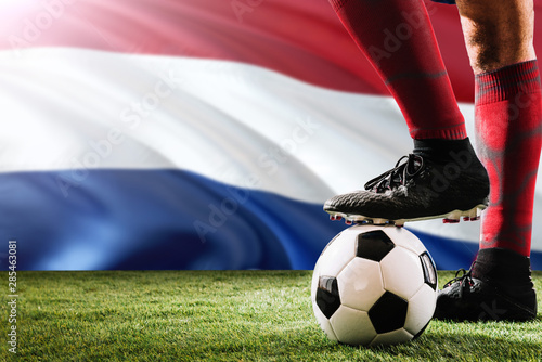 Close up legs of Netherlands football team player in red socks, shoes on soccer ball at the free kick or penalty spot playing on grass.
