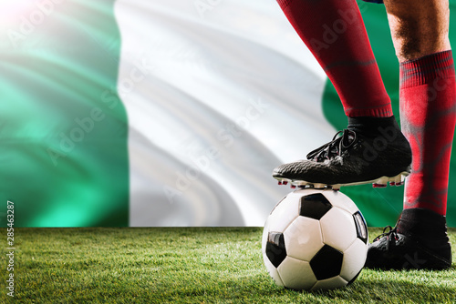 Close up legs of Nigeria football team player in red socks  shoes on soccer ball at the free kick or penalty spot playing on grass.