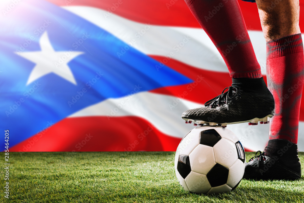 Close up legs of Puerto Rico football team player in red socks, shoes on soccer ball at the free kick or penalty spot playing on grass.