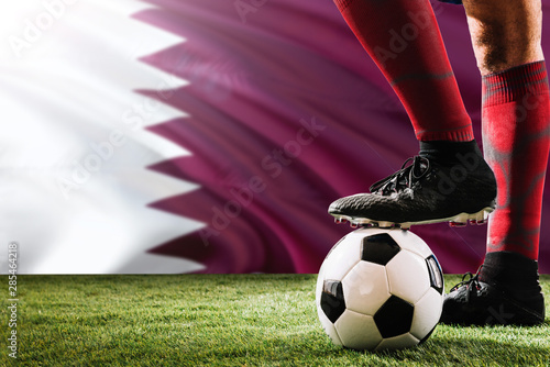 Close up legs of Qatar football team player in red socks, shoes on soccer ball at the free kick or penalty spot playing on grass. © sezerozger