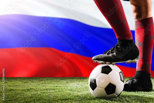 Close up legs of Russia football team player in red socks, shoes on soccer ball at the free kick or penalty spot playing on grass.