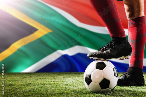 Close up legs of South Africa football team player in red socks, shoes on soccer ball at the free kick or penalty spot playing on grass.