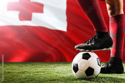 Close up legs of Tonga football team player in red socks, shoes on soccer ball at the free kick or penalty spot playing on grass.