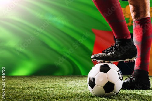 Close up legs of Zambia football team player in red socks, shoes on soccer ball at the free kick or penalty spot playing on grass. © sezerozger
