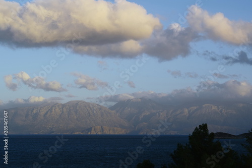 Blue sea and low mountains in the distance under a blue sky with white fluffy clouds, Crete
