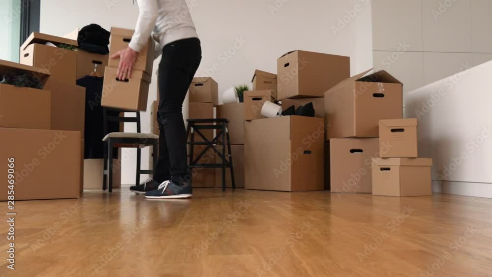 A moving man adds a cardboard box to a pile of other boxes in an empty apartment A moving man adds a cardboard box to a pile of other boxes in an empty apartment