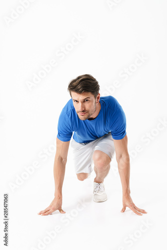 Handsome serious strong young sports man runner isolated over white wall background ready to run.