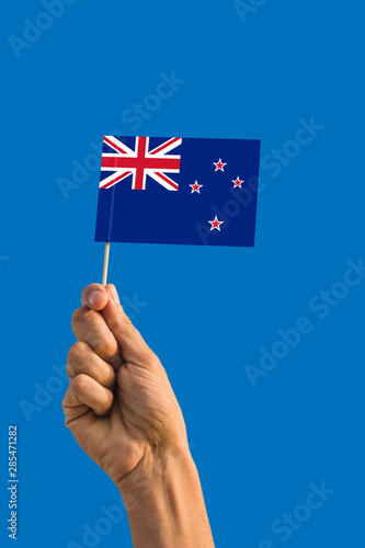 Woman hand holding New Zealand flag with stick, waving flag on deep blue sky. National theme, deep blue sky. © sezerozger