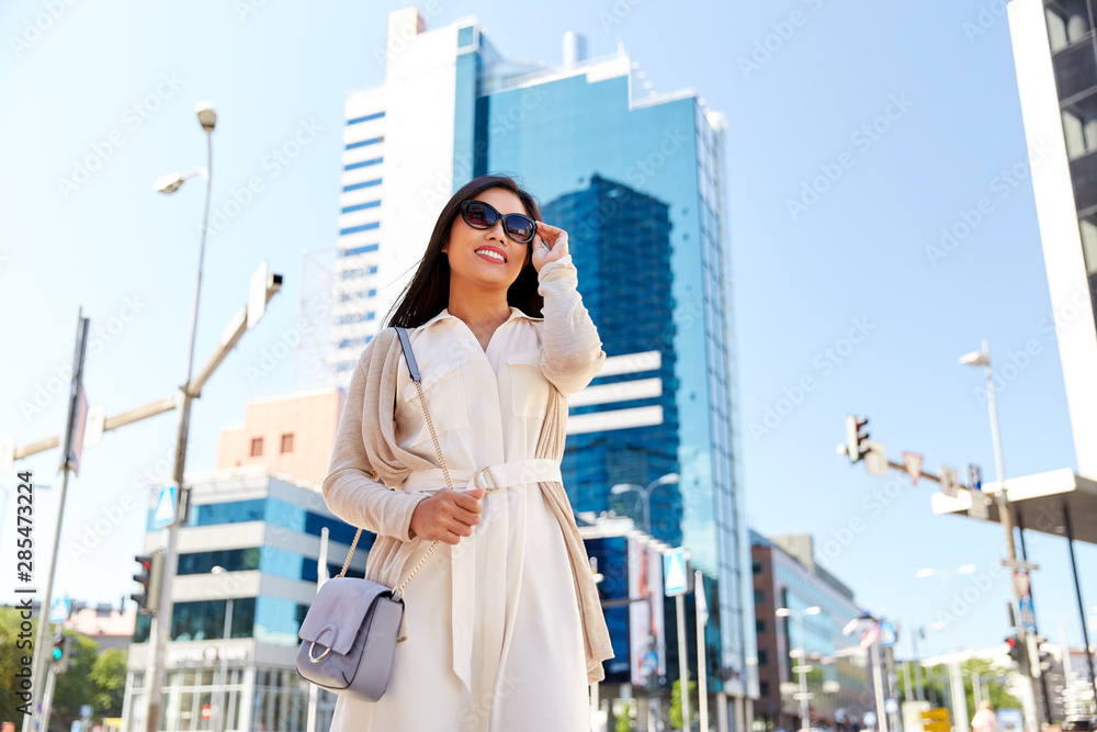 lifestyle and people concept - happy smiling young woman in sunglasses with handbag on city street