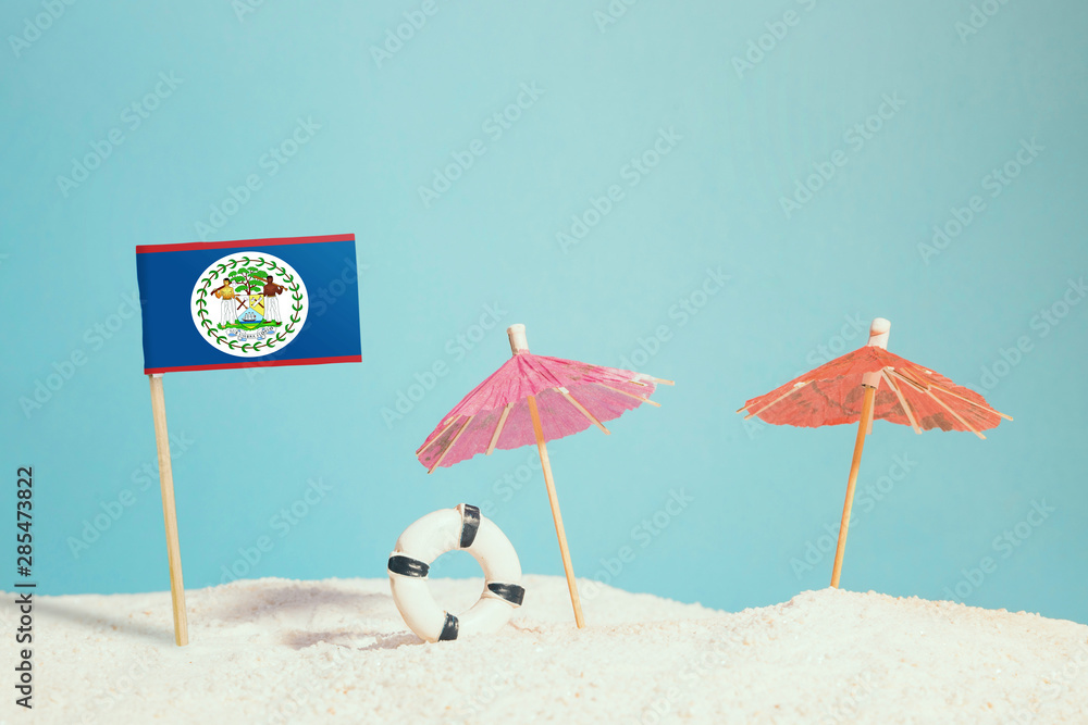 Miniature flag of Belize on beach with colorful umbrellas and life preserver. Travel concept, summer theme.
