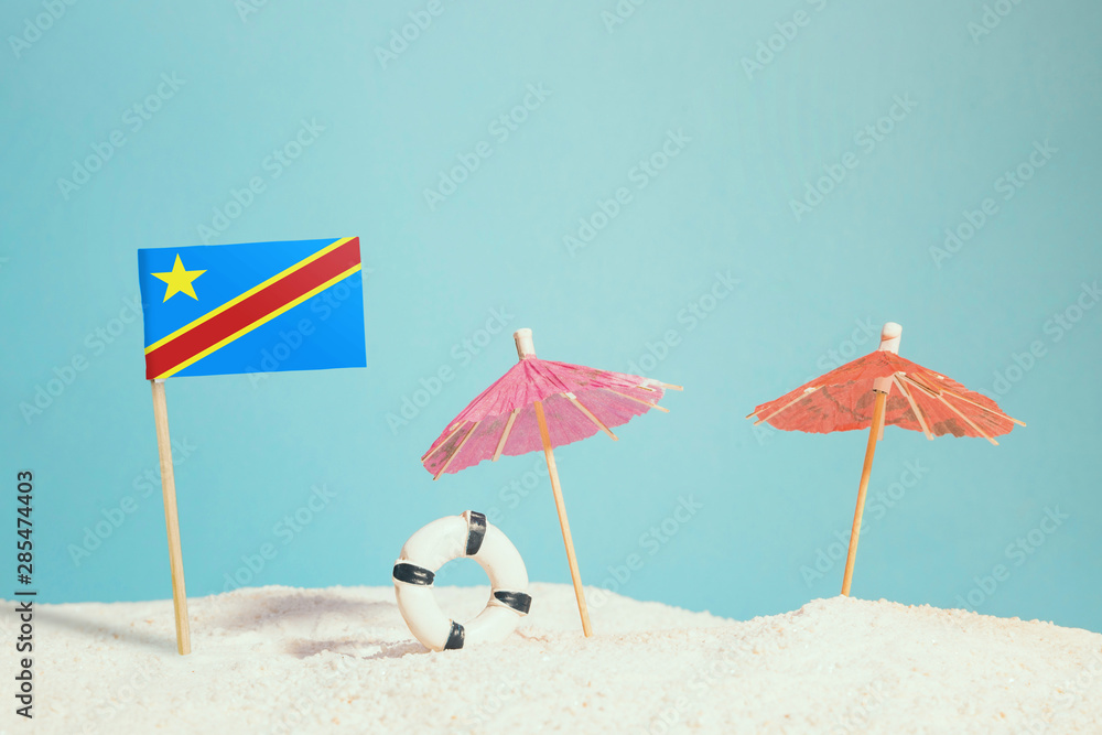 Miniature flag of Congo on beach with colorful umbrellas and life preserver. Travel concept, summer theme. Miniature flag of Congo on beach with colorful umbrellas and life preserver. Travel concept, summer theme.