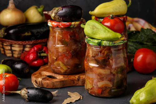 Vegetable salad with eggplant, onions, peppers and tomatoes in jars on a dark background, horizontal orientation