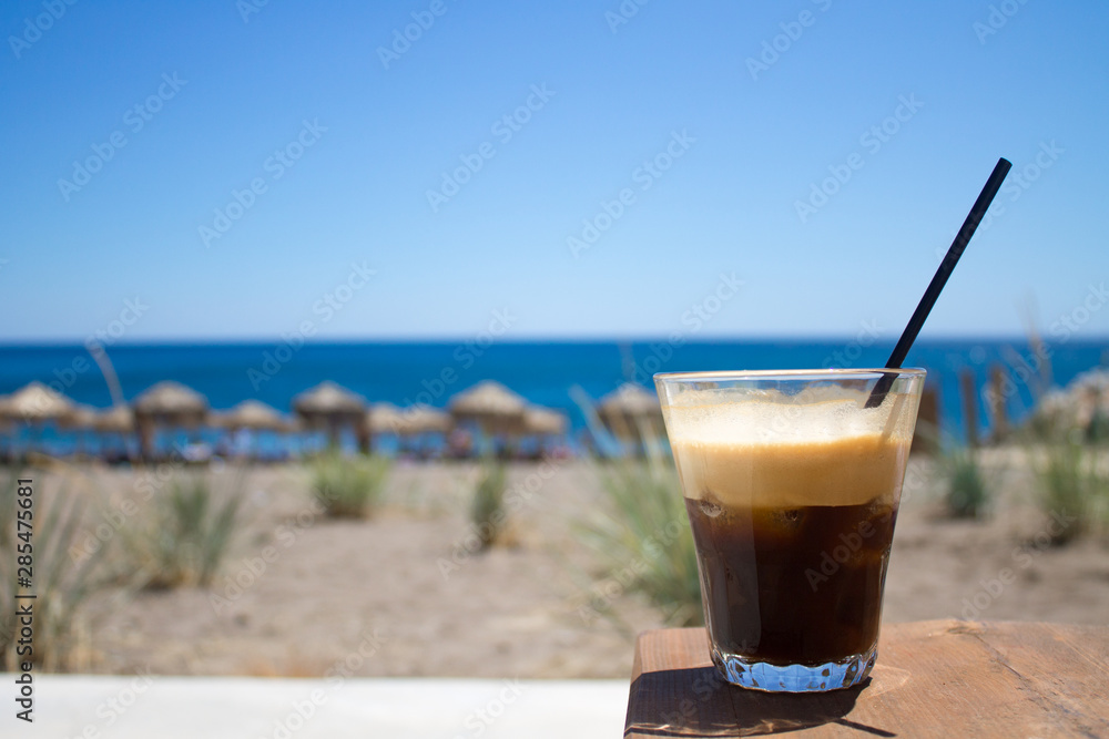 glass with ice coffee fredo espresso or frappe on the corner of the table with beach on background glass with ice coffee fredo espresso or frappe on the corner of the table with beach on background