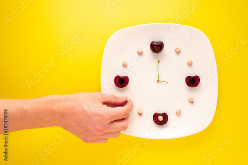 Symbolic clock mode of cherries and seeds with hand reaching for time. Art Time. photo