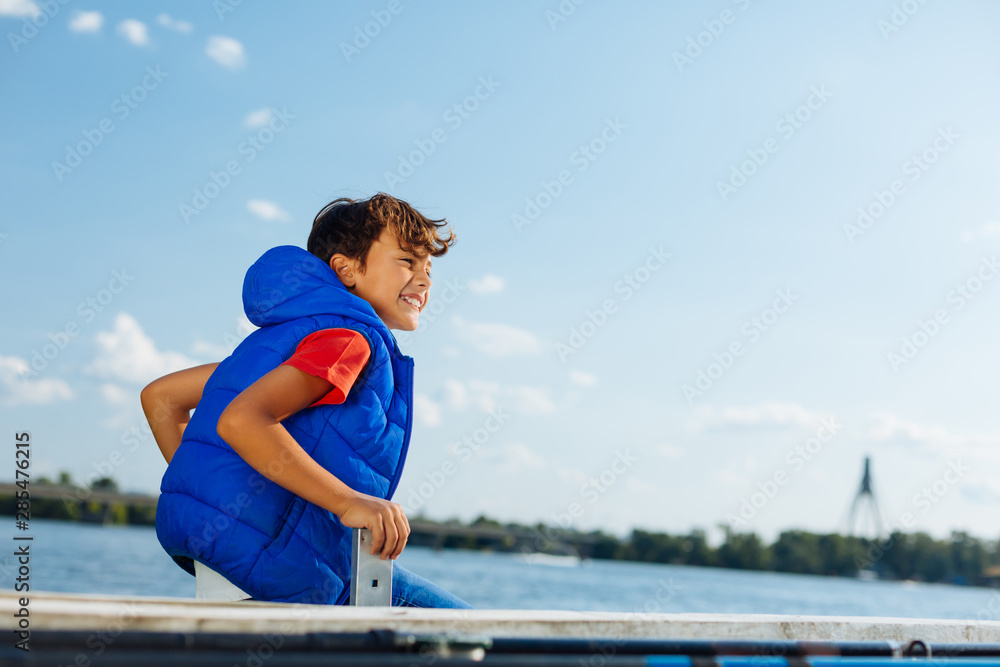 Cheerful boy sitting near river and enjoying the view Cheerful boy sitting near river and enjoying the view
