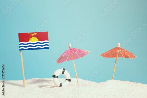 Miniature flag of Kiribati on beach with colorful umbrellas and life preserver. Travel concept  summer theme.