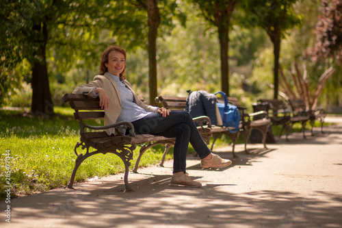one young lady, sitting in park on a bench, relaxing on a beautiful Spring day.