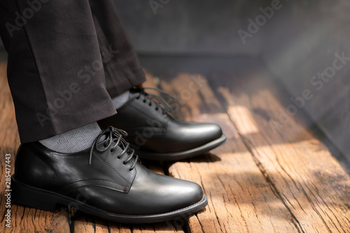 The men model wearing the gray trousers and black shoes leather on the wooden floor.