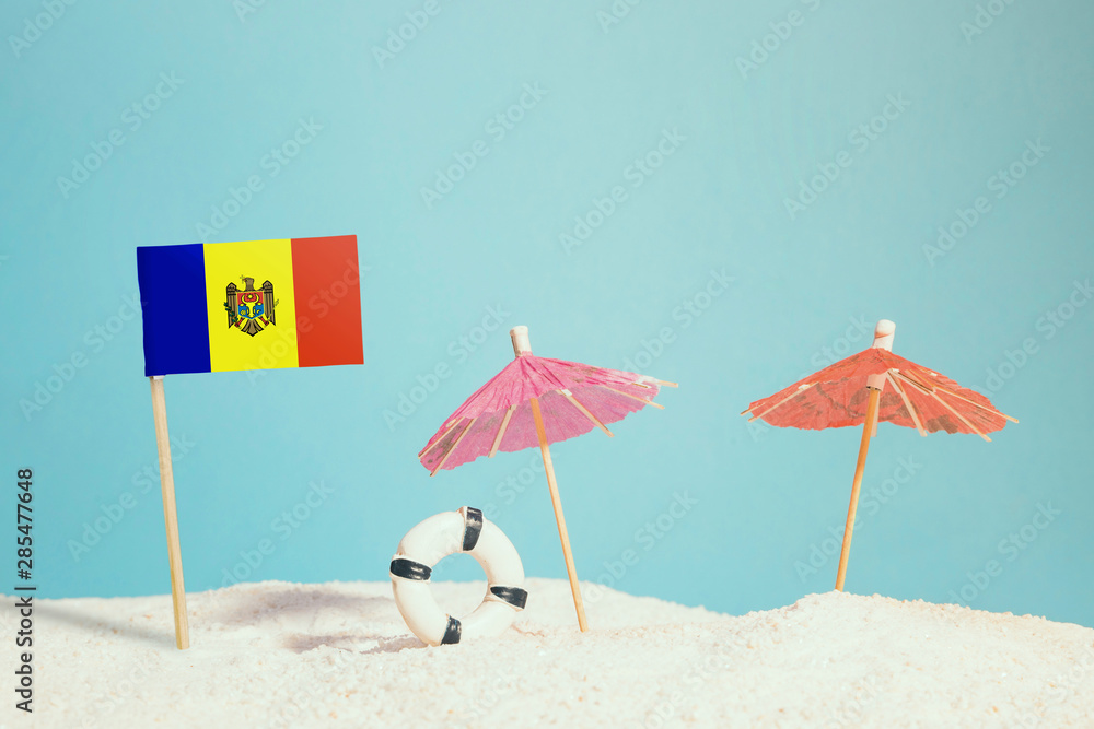 Miniature flag of Moldova on beach with colorful umbrellas and life preserver. Travel concept, summer theme.