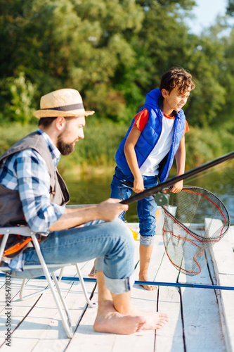 Dark-haired boy holding net while fishing with father