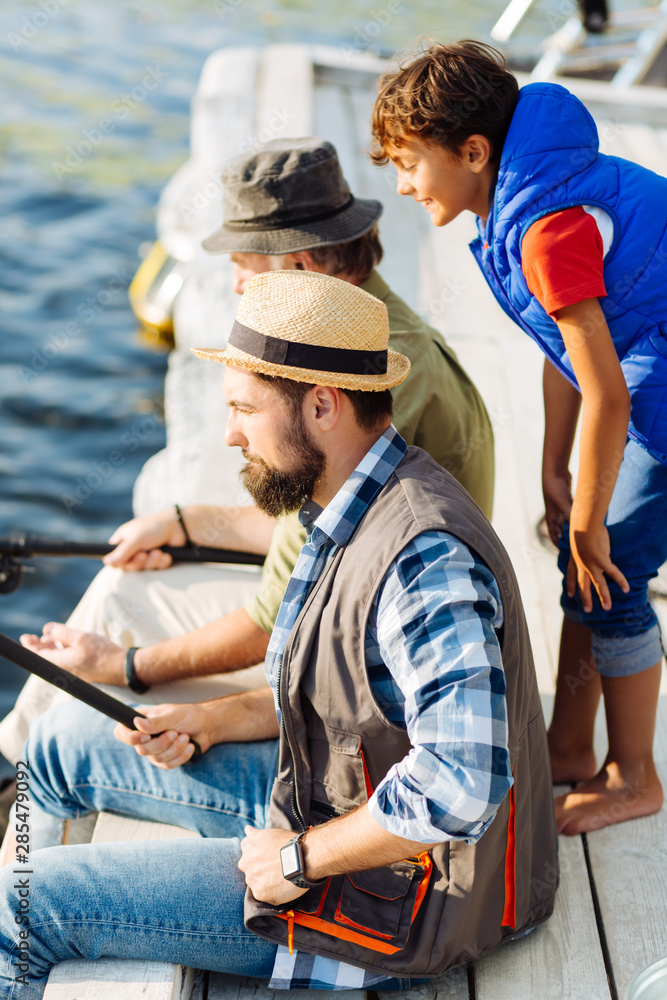 Curious boy watching his father and grandfather fishing