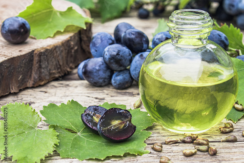 Grape seed oil in a glass bottle near blue grapes and green leaves on old wooden boards. Spa, eco products concept.