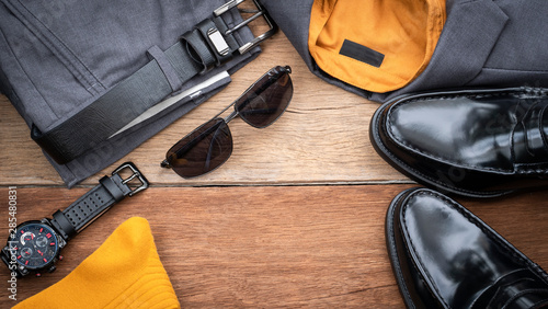 Men fashion casual clothing set on wooden background include penny loafer shoes, gray suit, yellow shirt, black watch, sunglasses, sock and belt. Flat lay, top view, copy space