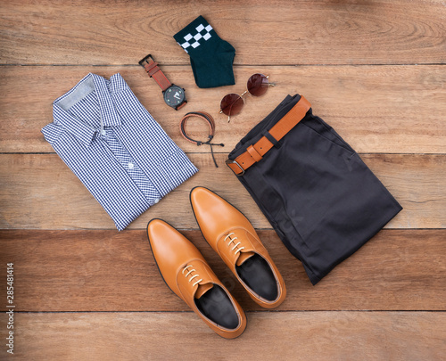 Flat lay, top view, men fashion casual clothing set on wooden background include oxford shoes, pants, belt ,watch, sunglass, green sock, bracelet and office shirt.