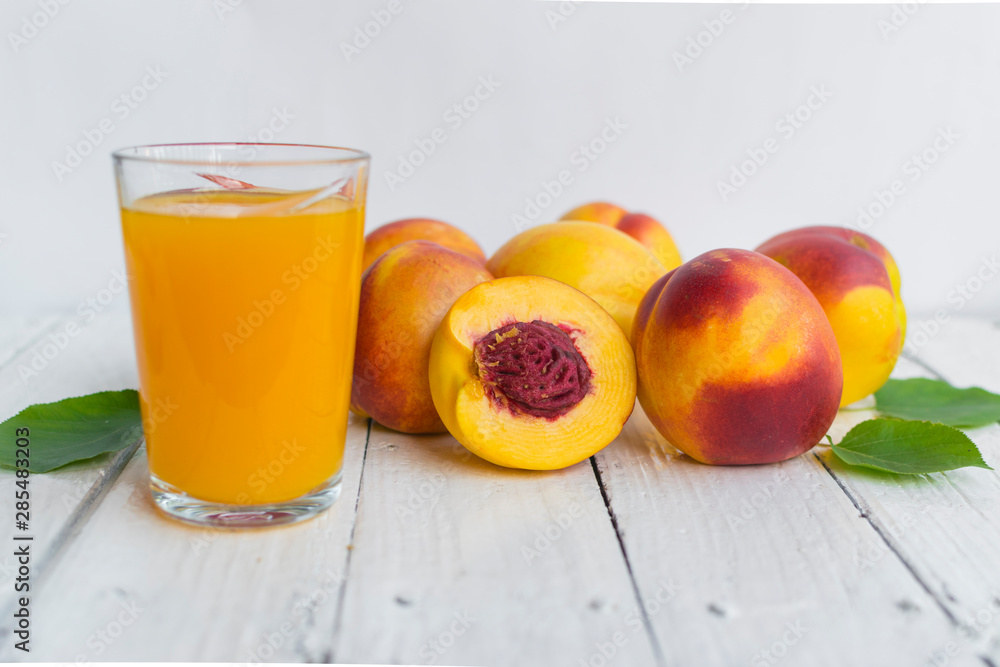 Delicious and juicy peach (nectarina) with glass of juice on white wooden table Delicious and juicy peach (nectarina) with glass of juice on white wooden table