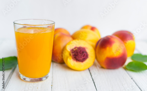 Delicious and juicy peach (nectarina) with glass of juice on white wooden table