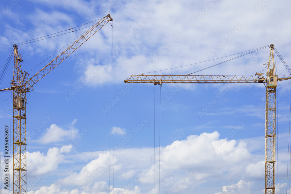 Copy space between two construction cranes against blue cloudy sky Copy space between two construction cranes against blue cloudy sky