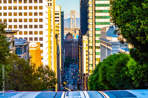 City street view in San Francisco, California uphill looking down between buildings and other architecture at Oakland Bay Bridge over the ocean. Unique American city on the west coast of United States photo