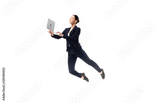 young cheerful businesswoman using laptop while levitating isolated on white photo