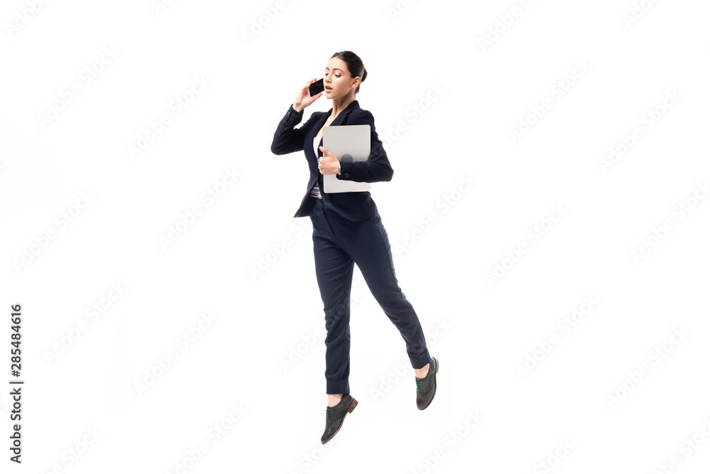 young businesswoman talking on smartphone and holding laptop while dancing isolated on white young businesswoman talking on smartphone and holding laptop while dancing isolated on white