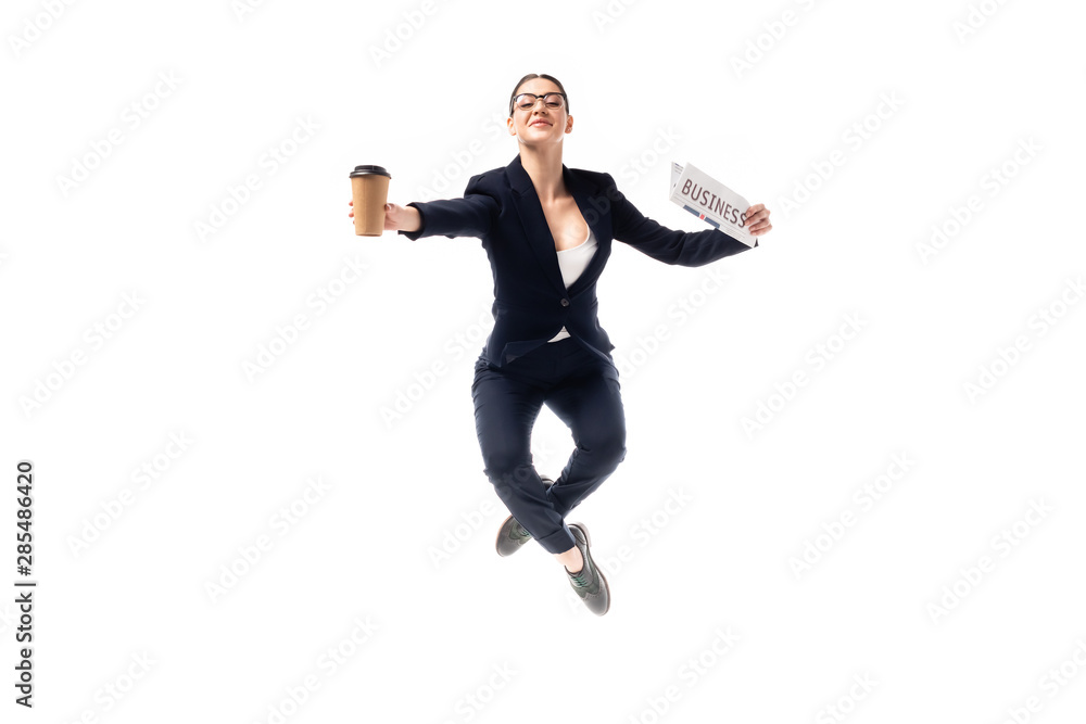 elegant businesswoman dancing while holding coffee to go and newspaper isolated on white