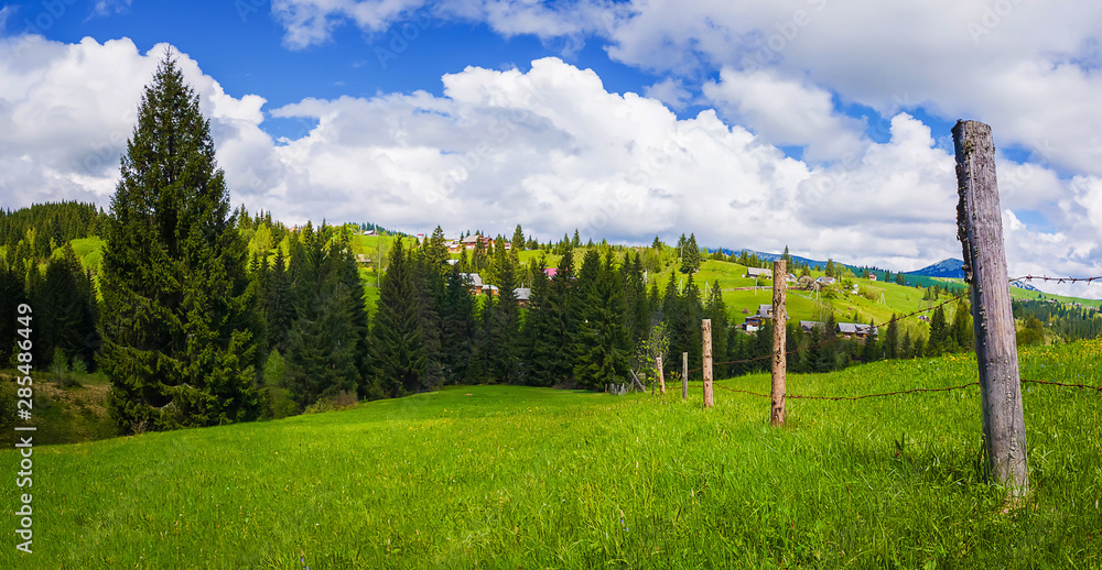 Typical Carpathians village landscape. Old fence made of wood pillars and barbed metallic wire across the farm on the green hills surrounded by coniferous forests